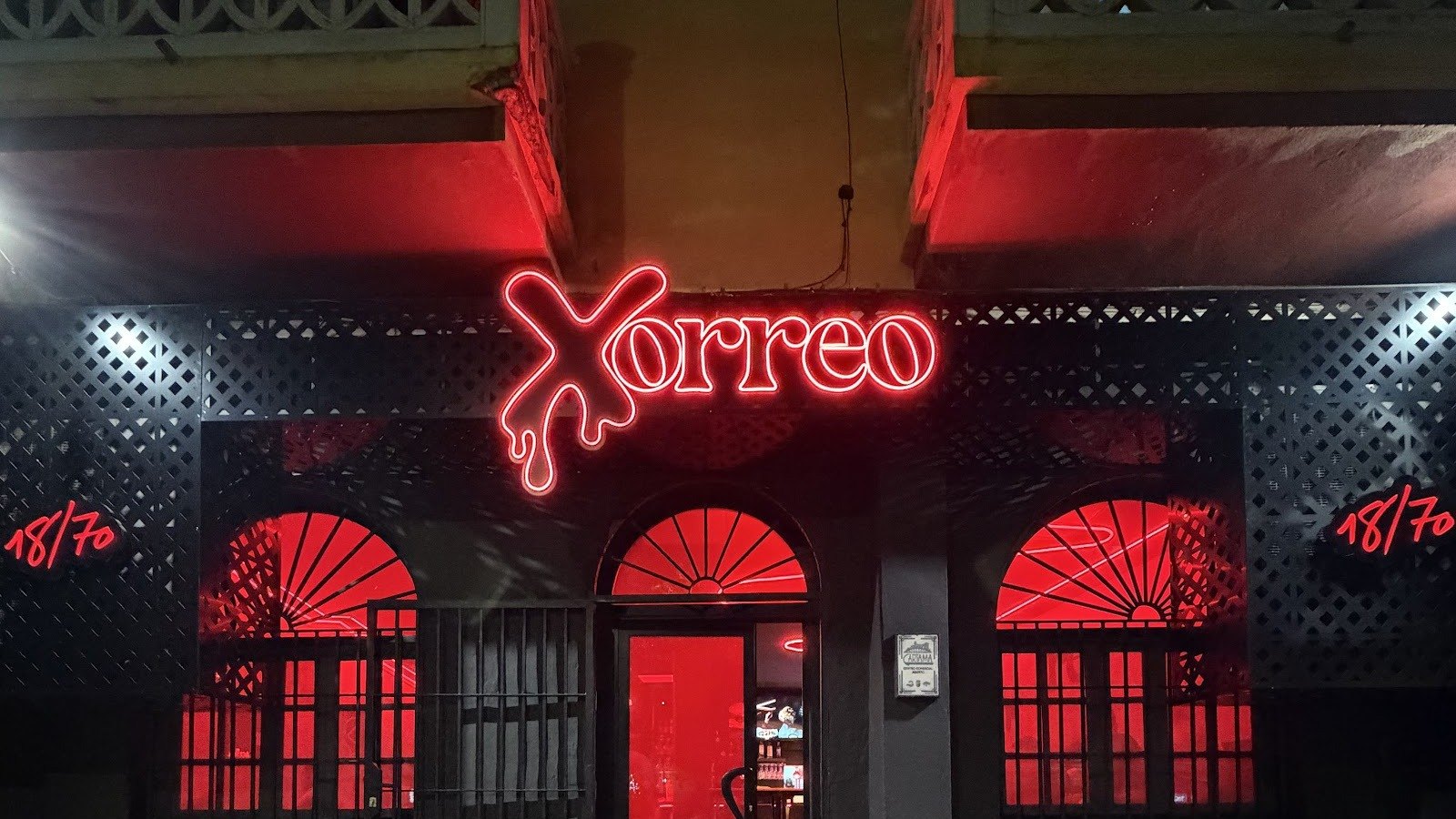Fachada nocturna de XORREO con el rótulo de neón rojo sobre la pared negra